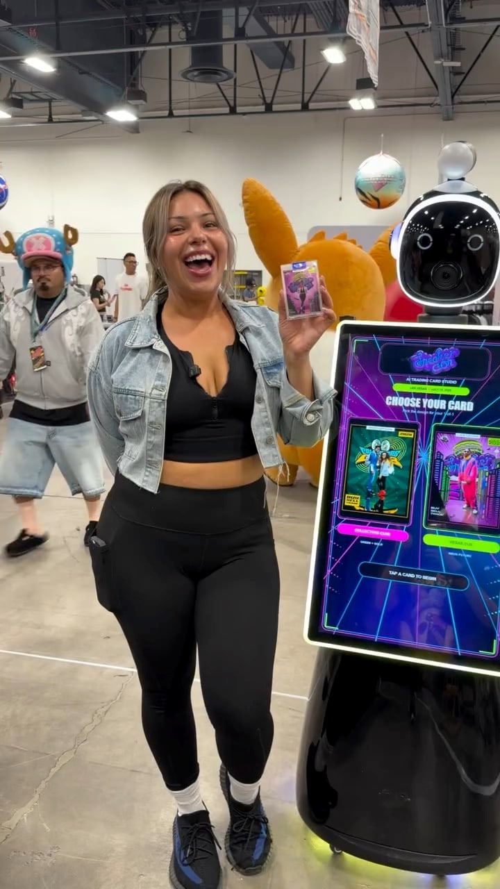 SneakerCon guest holding a finished card beside SnapBot Rosie